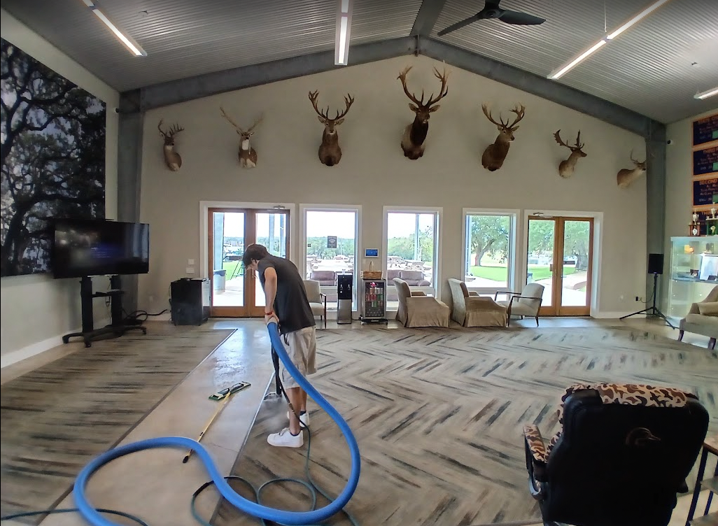 RJH and Sons technician steam cleaning a large stained concrete floor in a Hill Country event hall
