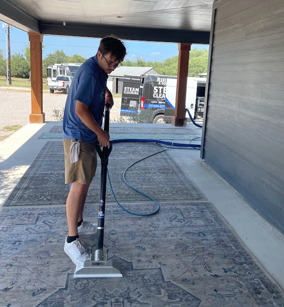 Paxon deep-cleaning a large area rug with a steam extraction wand in Dripping Springs, TX